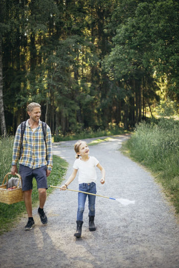 Smiling daughter talking to father holding picnic basket on road in forest
