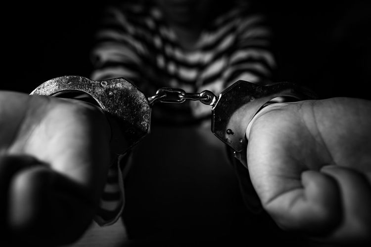 Midsection of prisoner with handcuffs over black background
