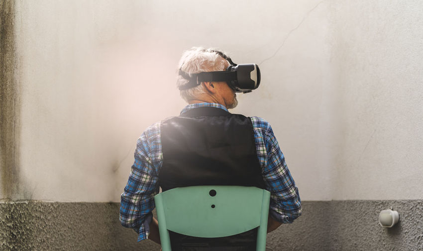 Rear view of senior man looking through virtual reality simulator while sitting on chair