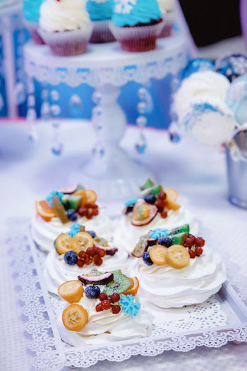 Cupcakes with white cream, garnished with berries and fruits, on a white tray with lace edges