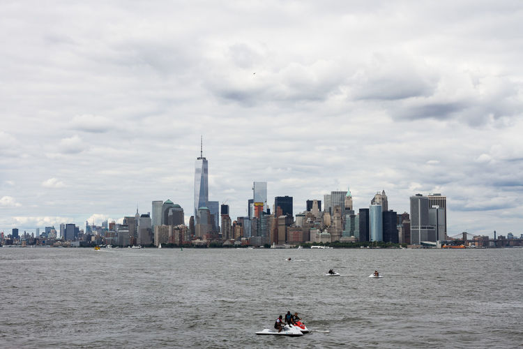 Men with jet skis in hudson river by manhattan against cloudy sky