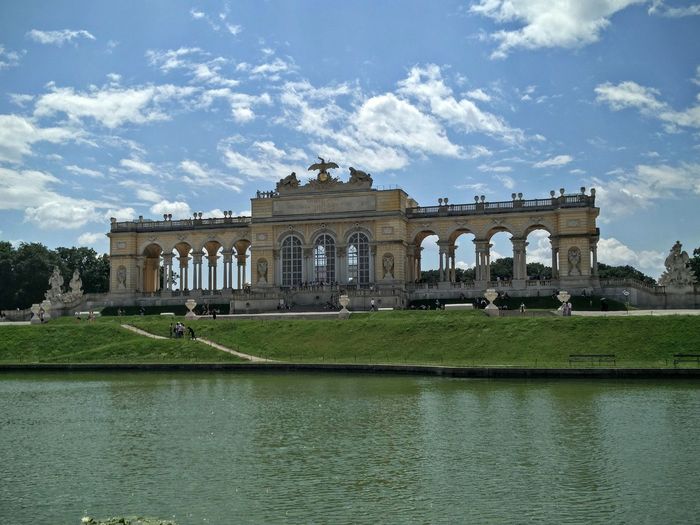 Schonbrunn palace in front of river against sky on sunny day