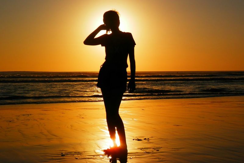 Silhouette woman standing at beach during sunset