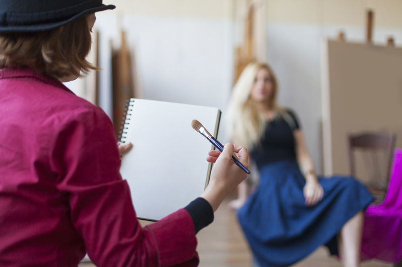 Woman painting while model sitting at studio