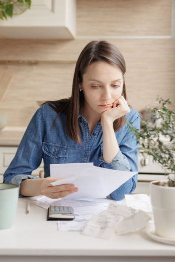 Sad young woman with documents sitting at table at home