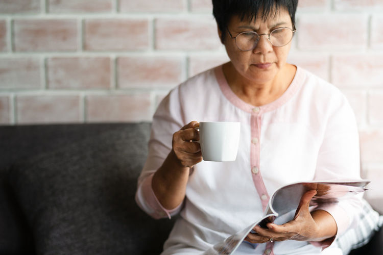 Old woman reading a book with cup of coffee at home