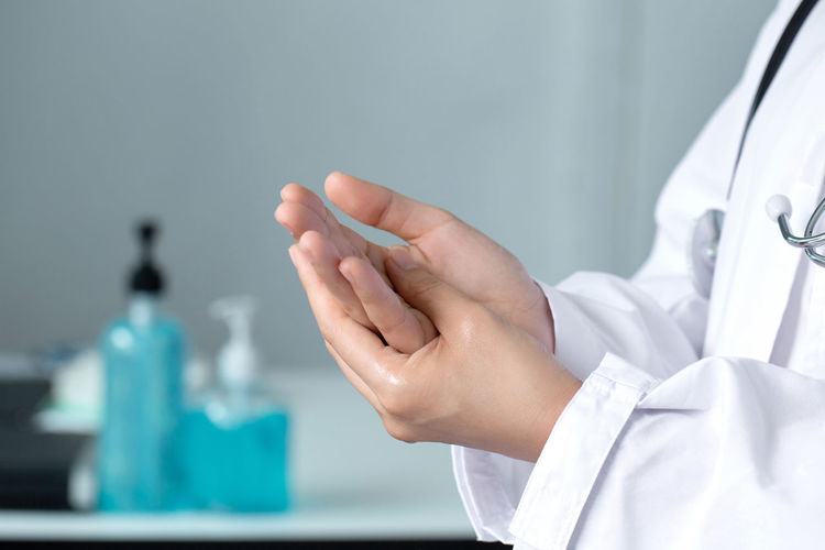 Midsection of doctor applying sanitizer on hands in office