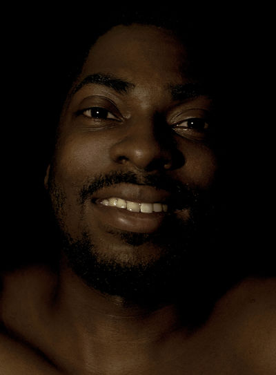 Close-up portrait of smiling young man against black background