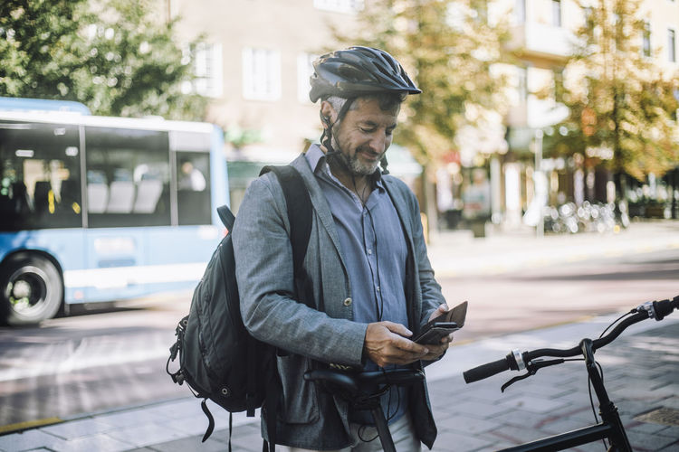 Smiling businessman wearing cycling helmet using mobile phone