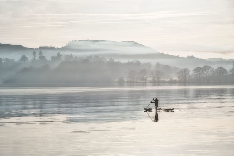 Peaceful paddleboarder on misty lake