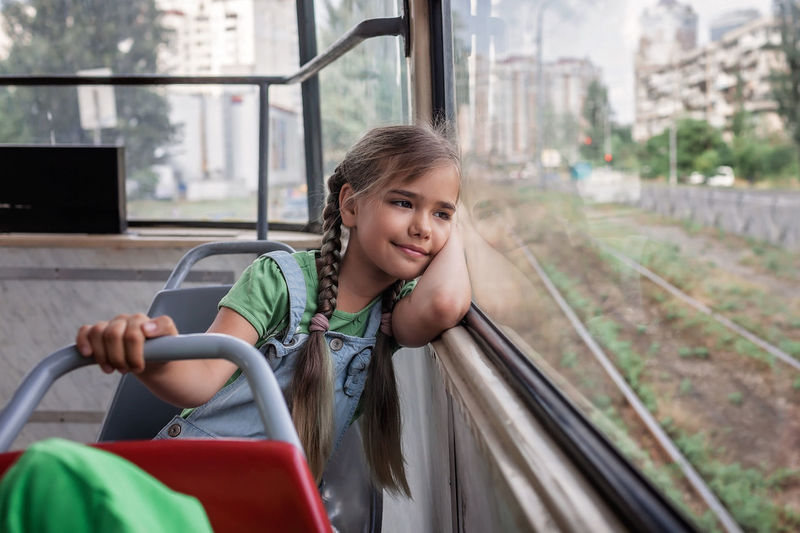 Young girl rides in empty tram and looks at the window dreamily, public transportation, city tramway