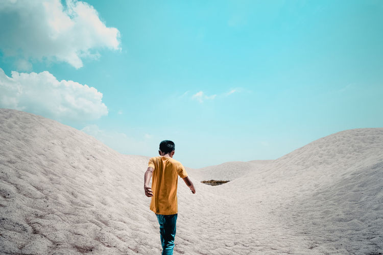 Rear view of boy walking at desert against blue sky