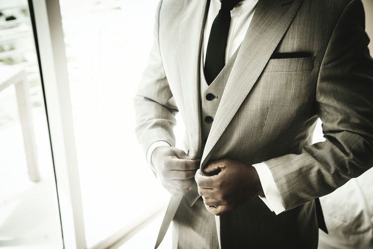 Midsection of man wearing suit by window