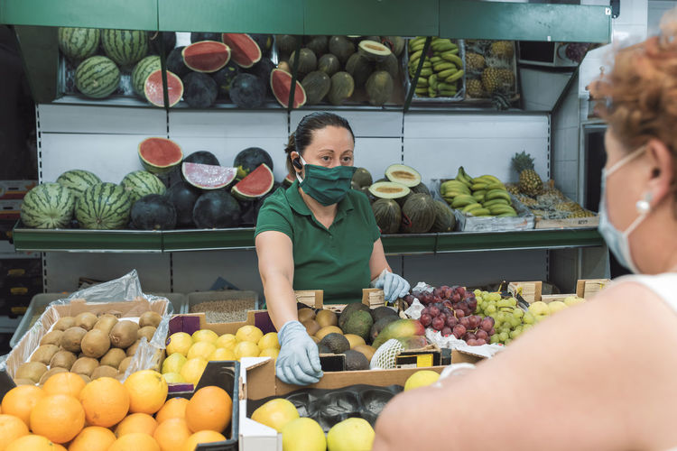 A shopkeeper with a mask attends to a customer in the greengrocer's.