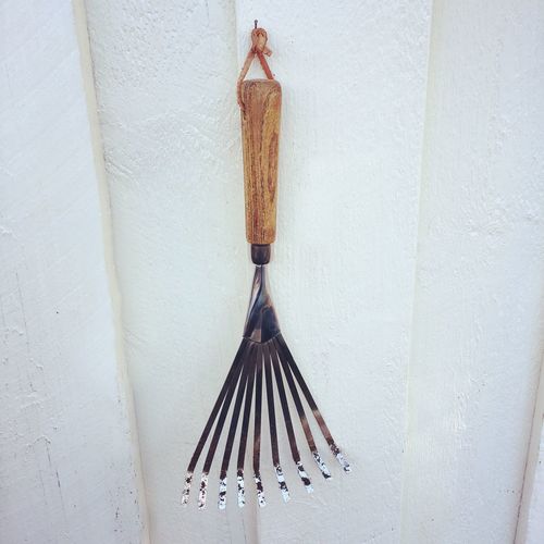 Close-up of small rake hanging on white wall