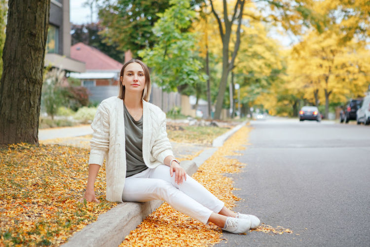 Beautiful middle age caucasian woman with short hair sitting in autumn fall street outdoor. 