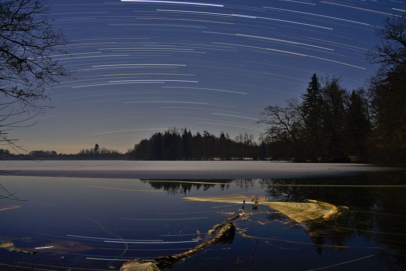 Star trails over lake against sky at night