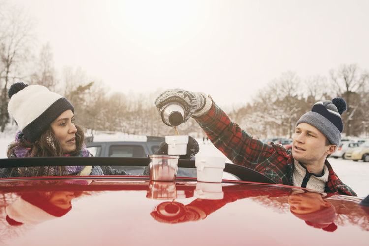 Friend looking at man pouring coffee in cup over car hood