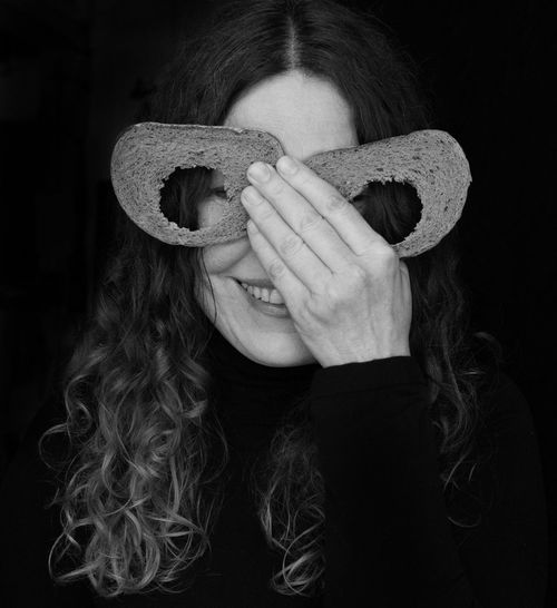 Portrait of woman covering eyes with bread slices against black background