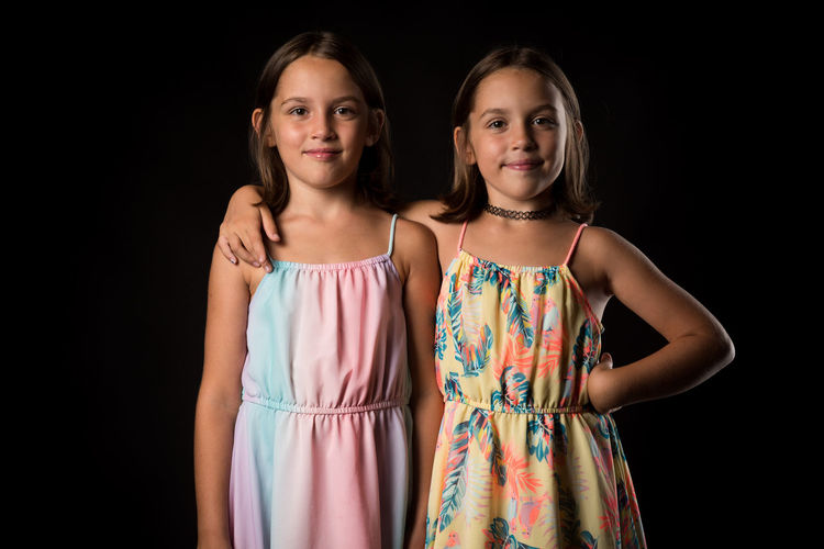 Portrait of girl standing with sister against black background