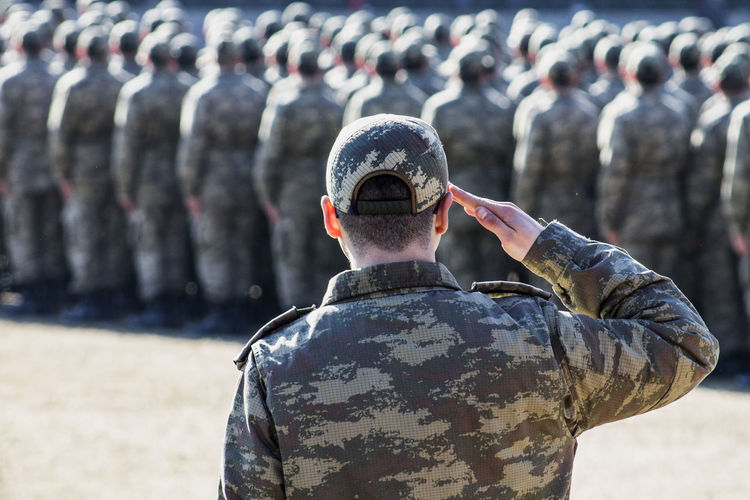 Rear view of soldier saluting outdoors