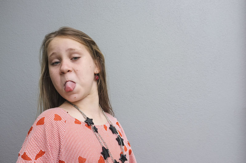 Close-up portrait of girl sticking out tongue against wall