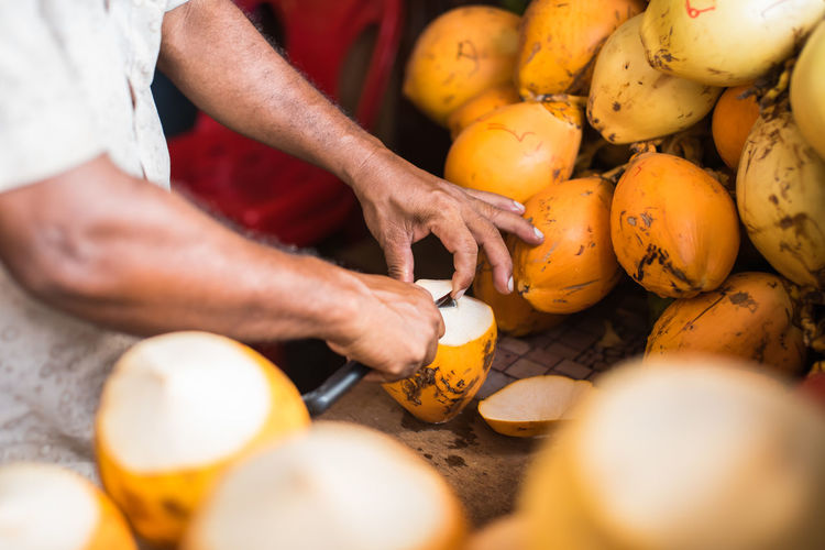 Midsection of vendor peeling coconuts at stall