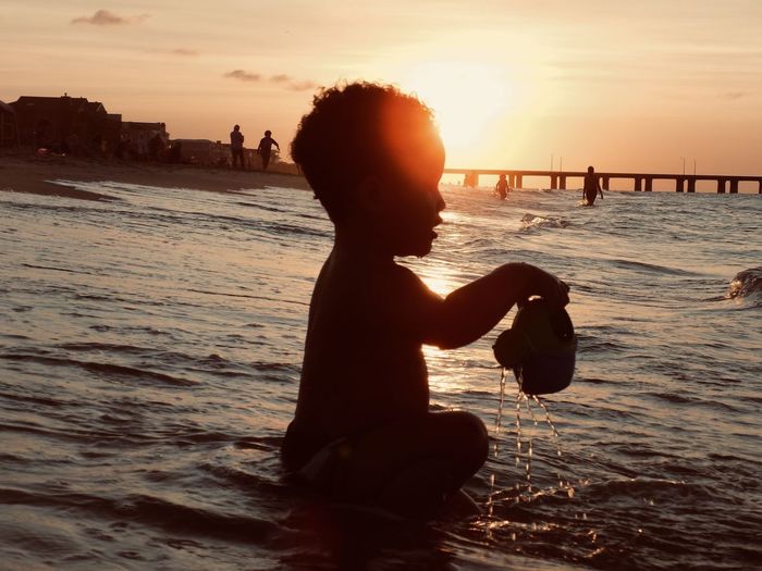  silhouette of little boy at beach, sun setting behind him.