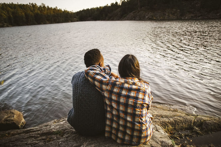 Rear view of man and woman sitting by lake in forest