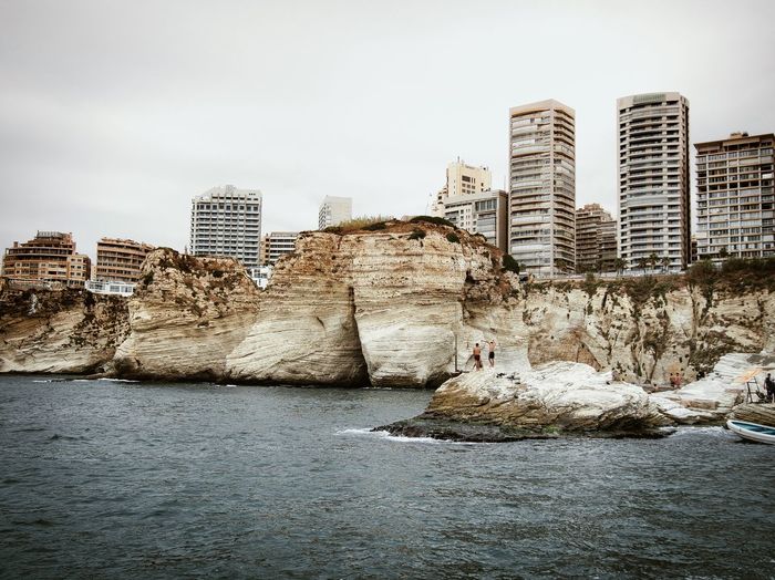 Sea by cliff against modern buildings in city