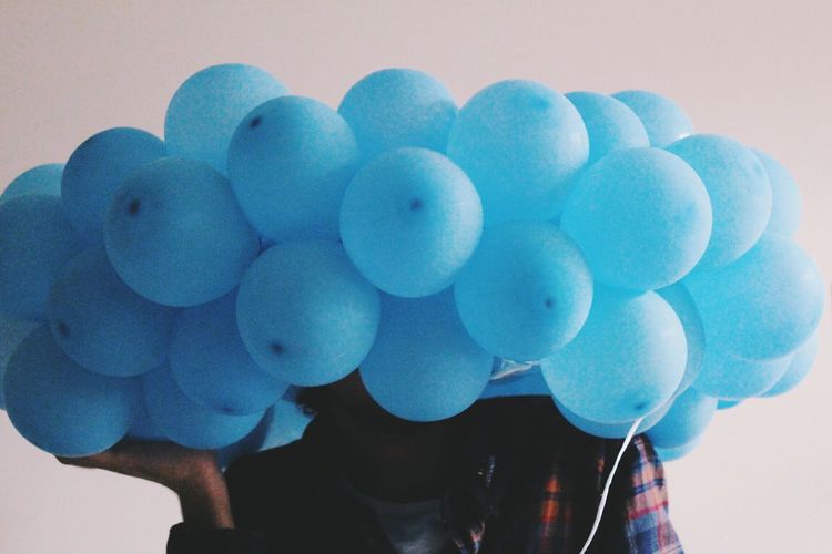 Close-up of man holding blue balloons in front of his head