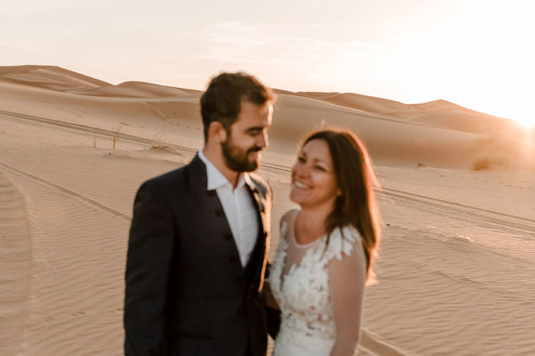 A couple in their wedding dresses in the desert are having fun while posing in the desert. 