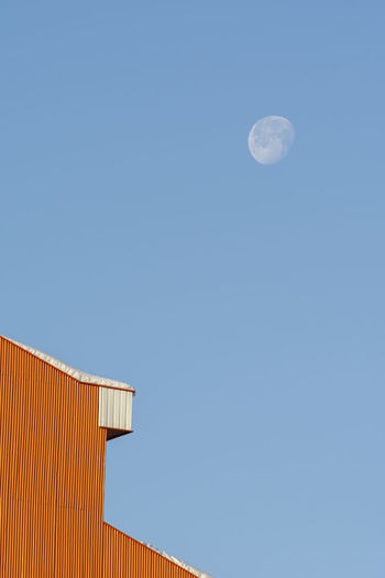 Detail shot of a house building rooftop after a snowfall in winter season, morning moon at blue sky