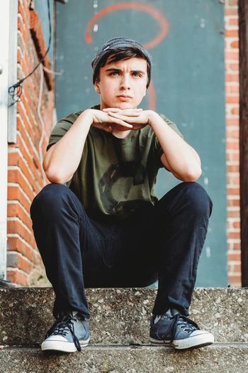 Portrait of young man sitting against wall
