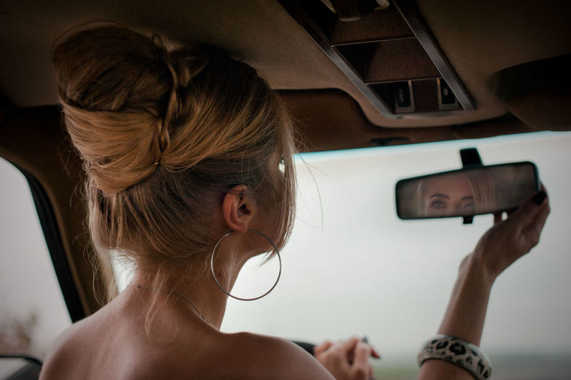 Rear view of woman holding mirror sitting in car