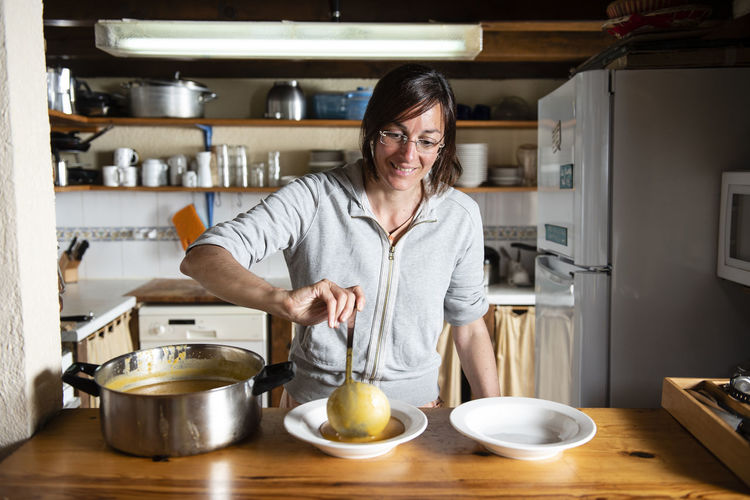 Woman serving a vegetable soup with pumpkin, potato and onion.