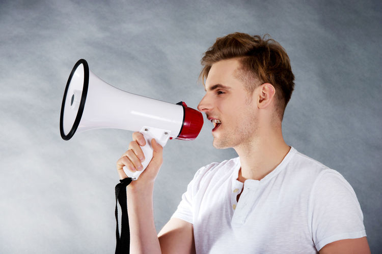 Young man with megaphone standing against gray backdrop