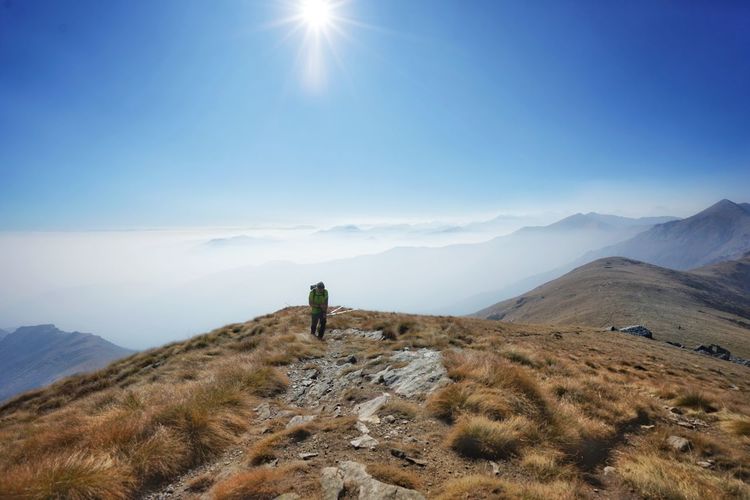 Hiker walking on mountain against blue sky