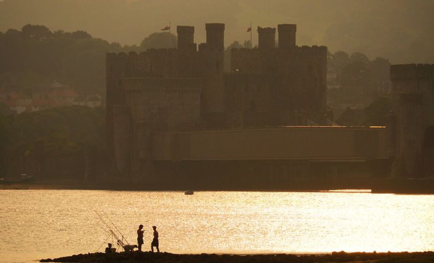 Two people in silhouette fishing with a castle in the background 