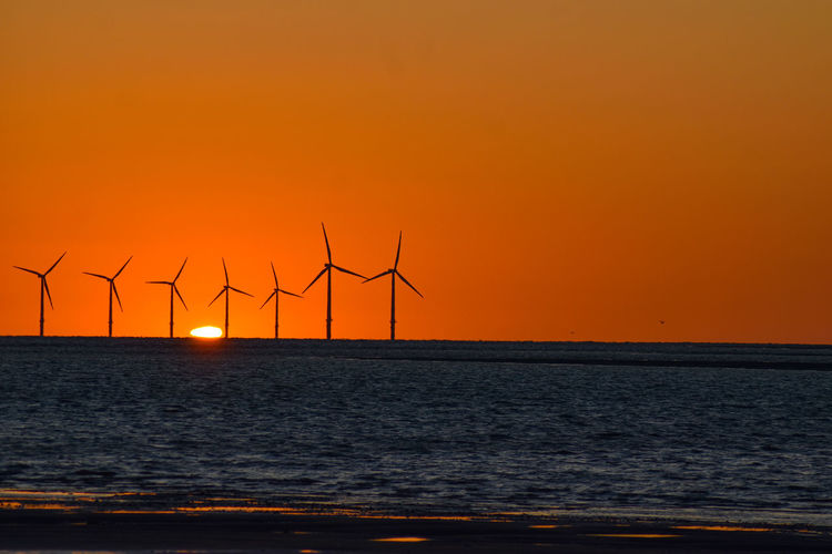 Wind turbines on sea against sky during sunset