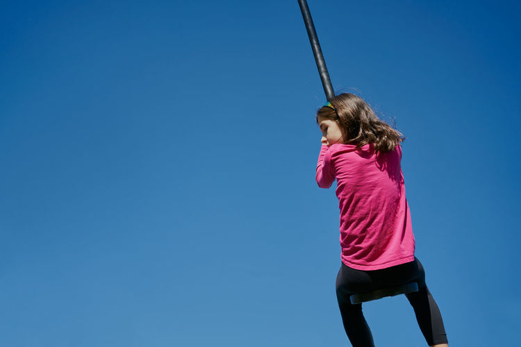 Low angle view of girl against clear blue sky