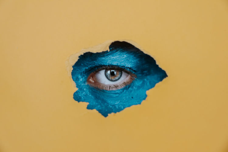 Close-up portrait of boy eye with face paint seen through paper hole