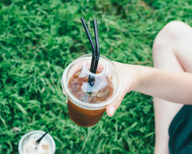 Cropped image of person holding latte at grassy field