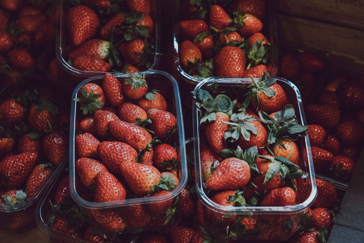 Top view of fresh strawberries on sale, portioned in plastic boxes, on top of a wooden table.