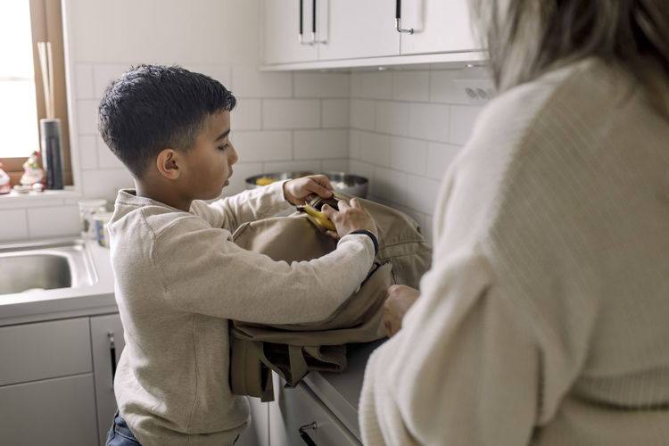 Autistic boy putting banana in bag standing by mother at home