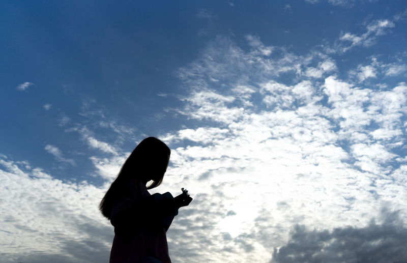 Low angle view of silhouette woman playing ukulele against sky