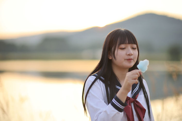 Portrait of young woman drinking water against lake