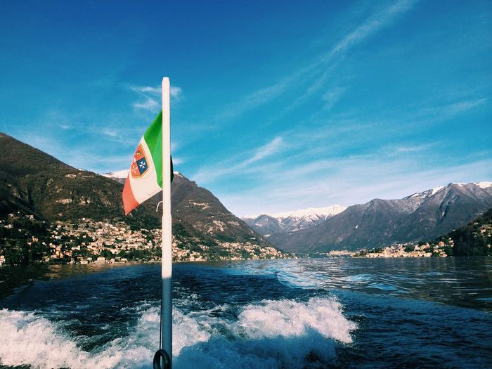 Flag on boat moving in lake against mountains