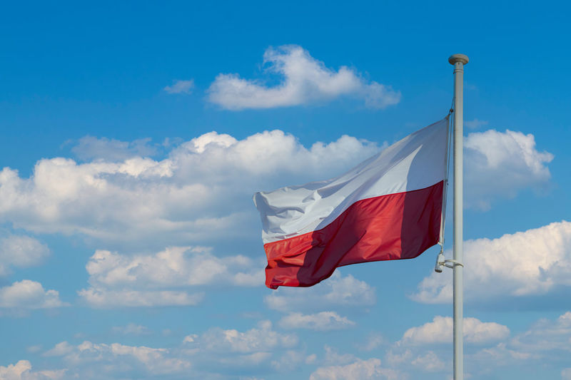 The national flag of poland flies against a blue sky and a few white clouds.