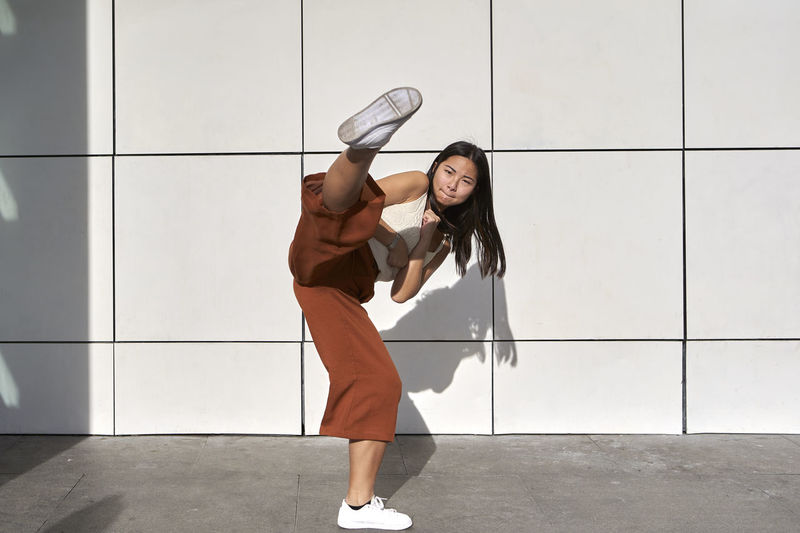 Young woman practicing kickboxing against wall